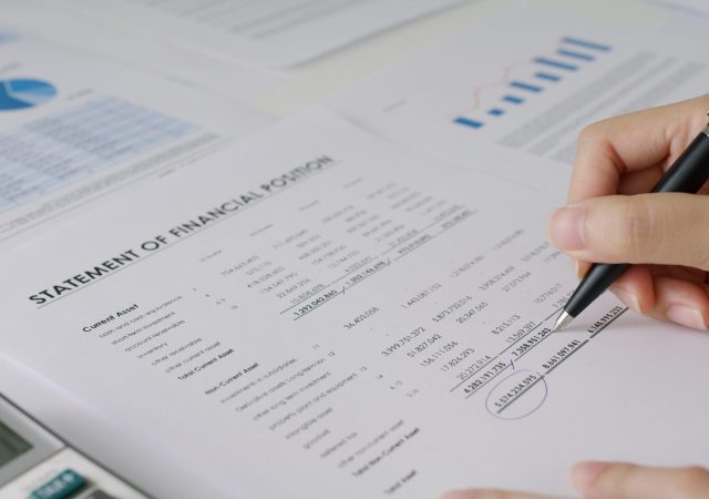 Close-up people hand of female stock trader use pen write on tax plan paper check number data income ledger in balance sheet at office. Budget control in audit clerk work for loan risk MBA learning.